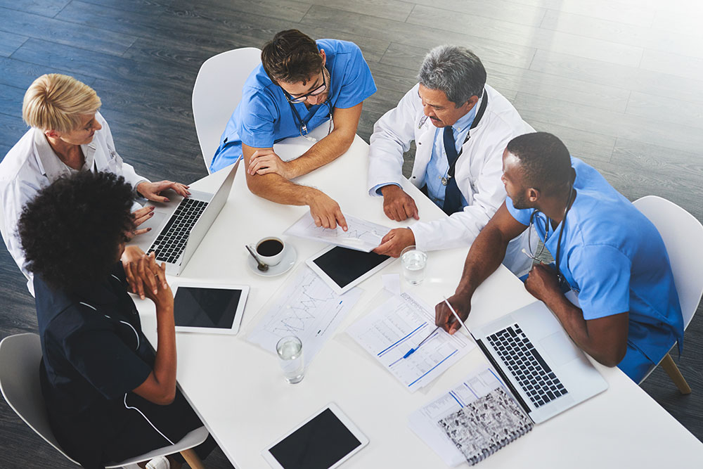 Team of medical workers sitting and meeting with laptops around table. Doctors and staff discussing papers and test results. Healthcare experts handling daily tasks and duties